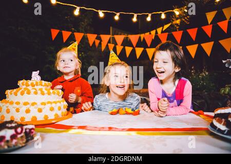 Kindergeburtstag. Drei fröhliche Kindermädchen am Tisch essen Kuchen mit den Händen und schmieren ihr Gesicht. Spaß Stockfoto