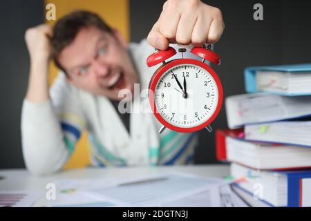 Mann schrie und hielt den roten Wecker am Tisch Nahaufnahme des Büros Stockfoto