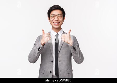 Waist-up-Porträt von zufrieden, voll zufrieden asiatischen jungen Mann in grauem Anzug, zeigt Daumen-up und lächelt mit Zustimmung, wie AW Stockfoto
