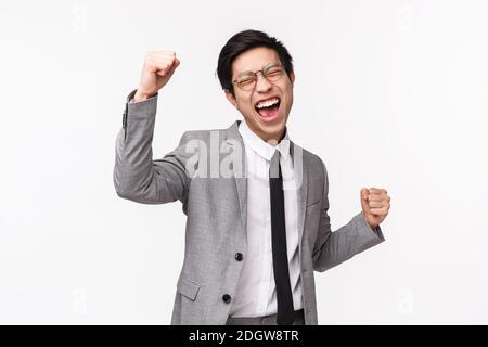Taille-up-Porträt erleichtert, erfolgreiche asiatische junge Geschäftsmann, männliche Unternehmer in grauem Anzug, Faust Pumpe, tun Champion Tanz, Stockfoto
