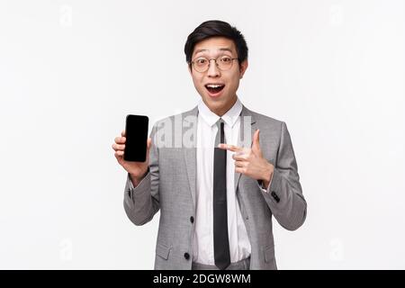 Waist-up-Porträt von erstaunt und aufgeregt asiatischen jungen Büroangestellte zeigt etwas genial auf Smartphone-Bildschirm, halten mobilen ph-wert Stockfoto