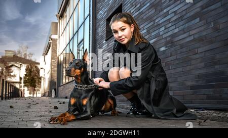 Teenager Mädchen neben einem Hund auf der Straße sitzen. Mädchen umarmt ihren Hund in der städtischen Umgebung. Verbringen Sie Freizeit zusammen Stockfoto