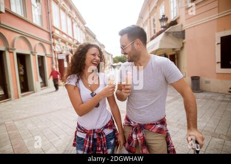 Junge wunderschöne Paar steht auf der Straße lacht miteinander und isst Eisreams. Stockfoto