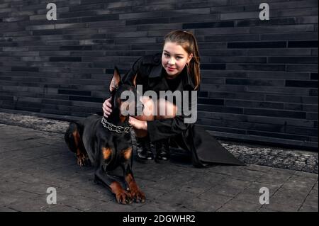 Teenager Mädchen neben einem Hund auf der Straße sitzen. Mädchen umarmt ihren Hund in der städtischen Umgebung. Verbringen Sie Freizeit zusammen Stockfoto