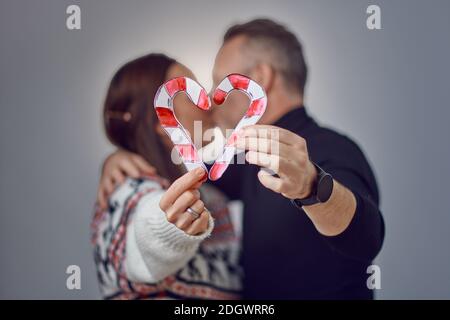 Incognito verheiratet erwachsenen Paar küssen und zeigt die herzförmige Figur der Süßigkeiten Süßigkeiten Süßigkeiten. Weihnachten Urlaub liebevolle Familienportrait im Studio Stockfoto