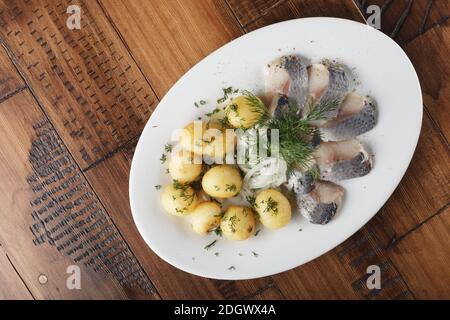 Heringsfisch mit jungen Kartoffelbällchen auf weißem Teller. Holzhintergrund. Stockfoto