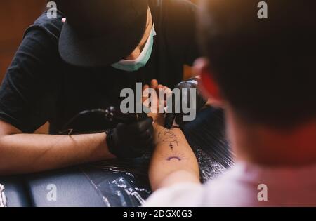 Junge fokussierte Tattoo-Künstler färben Kunden Arm sorgfältig in seinem Shop. Stockfoto