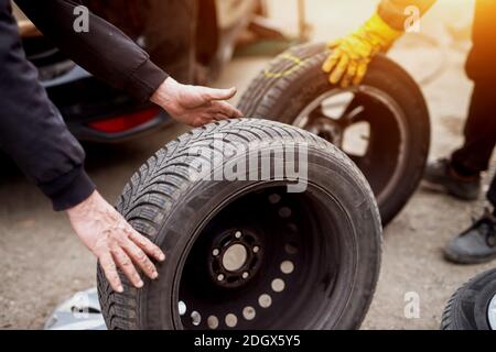 Zwei Mechaniker schieben Räder aufeinander zu und ersetzen altes mit neuem an einem Auto. Stockfoto