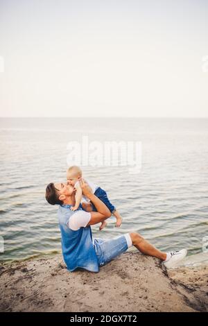 Sommerurlaub mit der Familie in der Natur. Vater und kleine Tochter sitzen ein Jahr lang auf einer sandigen Klippe mit Blick auf das Meer. Ein Mann ist es Stockfoto