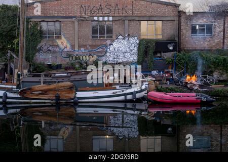 Industrielager, Lagerfeuer, rassistische Street Art, verödselte Land- und Flussboote auf dem Lea Valley Kanal, London, Großbritannien Stockfoto