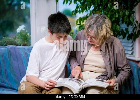 Eine Großmutter und ein Enkel lesen zusammen auf einem Sofa Ein häuslicher Wohnraum Stockfoto