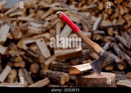 Eine hölzerne, alte Axt in ein gesägtes, altes Stück Holz vor dem Hintergrund des gehackten Brennholzes eingefügt. Stockfoto