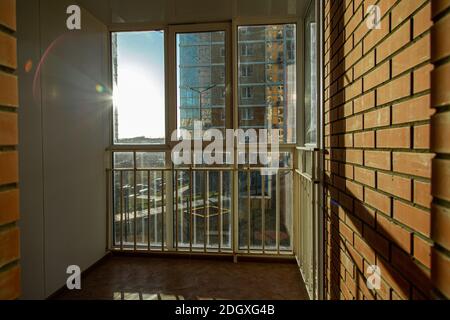 Die helle Sonne scheint wunderschön durch das Fenster auf dem Balkon mit Bars und Kunststofffenstern. Werfen Sie einen Schatten auf eine Ziegelmauer. Stockfoto