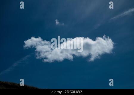 Definierte einzelne weiße Wolke auf einem tiefblauen Himmel Stockfoto