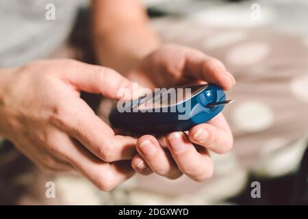 Thema Diabetes. Ein Makroplan für Nahaufnahmen. Hände einer jungen kaukasischen Frau zu Hause im Schlafzimmer auf dem Bett. Es verwendet das Technolog Stockfoto