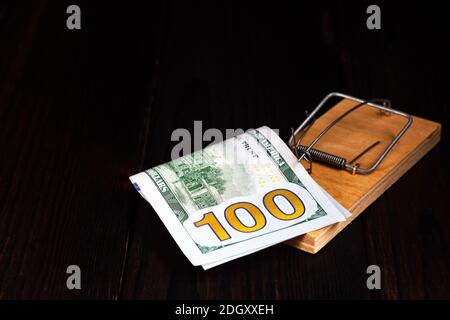 Hundert-Dollar-Schein in einer Mausefalle auf einem dunklen Holzhintergrund. Stockfoto