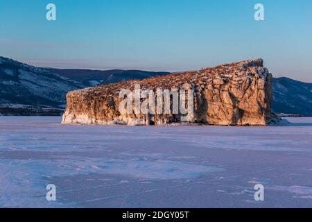 Fantastischer Sonnenuntergang mit Blick auf eine hell erleuchtete Insel im Winter auf dem Eis des Baikalsees, Sibirien Russland. Wintersaison Naturlandschaft. Speicherplatz kopieren. Stockfoto