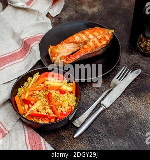 Frisch gegrillter Lachs und Bulgur mit Gemüse in schwarzer Schüssel Stockfoto