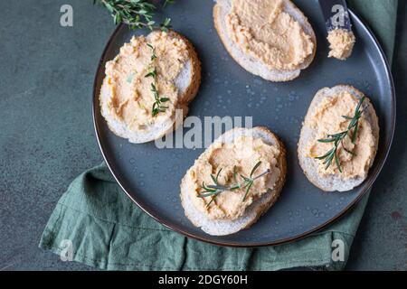 Sandwiches mit geräuchertem Lachs und weicher Frischkäse-Pastete oder Mousse mit Thymian und Rosmarin auf einer Keramikplatte, grüner Betonboden. Selektive Stockfoto