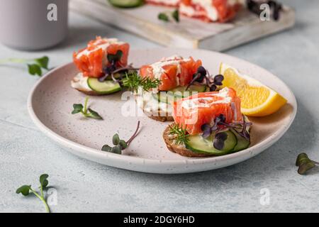 Mini-Sandwiches mit geräuchertem Lachs, Frischkäse, Gurke und Microgreen auf Roggenbrot, grauer Steinhintergrund. Vorspeise mit Lachs und Käse c Stockfoto