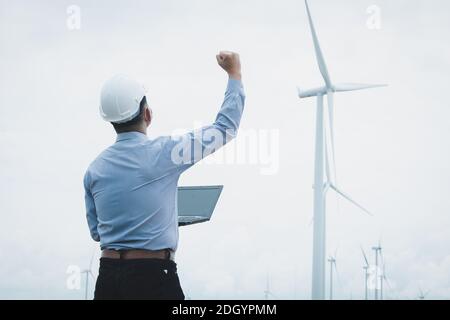 Ingenieure Windmühlen tragen Gesichtsmaske und arbeiten auf Laptop mit Die Windenergieanlage im Hintergrund Stockfoto