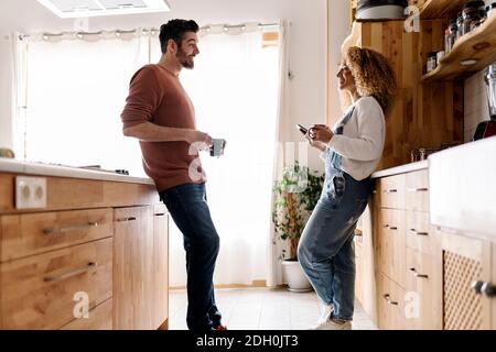 Stock Foto von einer Frau und einem Mann mittleren Alters, die in einer Küche stehen und lachen. Die Frau schaut auf den Mann. Sie lachen. Stockfoto