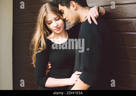 Portrait eines attraktiven Mischvolkspaares, das vor dem Hintergrund einer Holzwand zusammensteht. Dating, multiethnisches Tragen Stockfoto