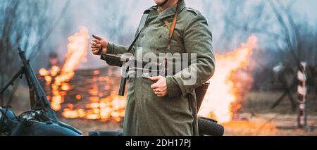 Re-enactor gekleidet als deutscher Wehrmacht Infanterie-Soldat im Zweiten Weltkrieg steht vor dem Hintergrund EINES brennenden Hauses. Deutscher Soldat des Zweiten Weltkriegs Stockfoto