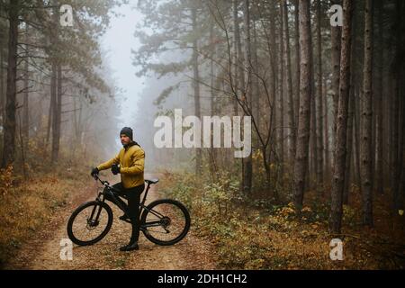 Schöner junger Mann, der beim Radfahren durch den Herbst eine Bremse zieht Wald Stockfoto