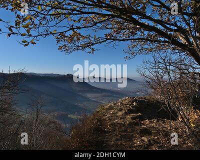 Atemberaubende Aussicht auf die Ausläufer der Schwäbischen Alb mit Burg Hohenneuffen in der Morgensonne im Spätherbst mit Schatten und trüber Luft. Stockfoto