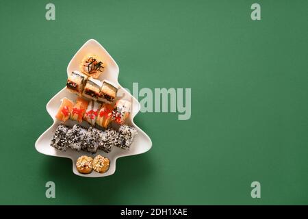 Sushi-Set in Teller als Weihnachtsbaum auf grünem Hintergrund dekoriert. Blick von oben. Leerzeichen für Text. Flatlay-Style. Stockfoto