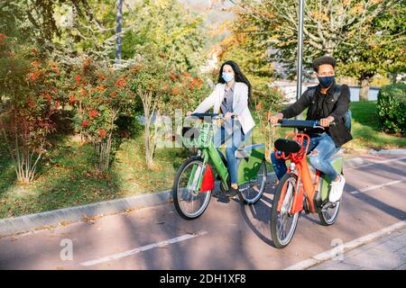 Vor zwei jungen Mann und Frau reiten entlang ein Fahrradweg mit einem gemeinsamen Elektro-Fahrrad in einem schönen park mit vielen Bäumen bei Sonnenuntergang tragen ein f Stockfoto