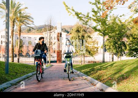 Vor zwei jungen Mann und Frau reiten entlang ein Fahrradweg mit einem gemeinsamen Elektro-Fahrrad in einem schönen park mit vielen Bäumen bei Sonnenuntergang tragen ein f Stockfoto