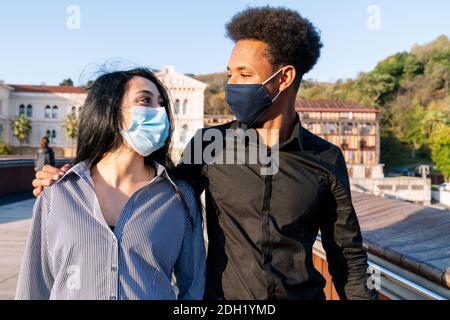 Porträt eines jungen Paares, das die Straße entlang umarmt Ein glücklicher blauer Himmel am Valentinstag mit einem Gesicht Maske aufgrund des Coronavirus 2020 covid-19 Stockfoto