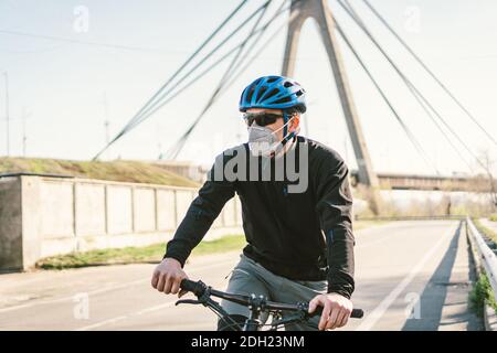 Männlicher Radfahrer trägt Atemschutzmaske mit strapazierfähigem Schutzfilter. Mann auf dem Fahrrad trägt Atemschutzmaske Gesichtsmaske mit schweren Stockfoto