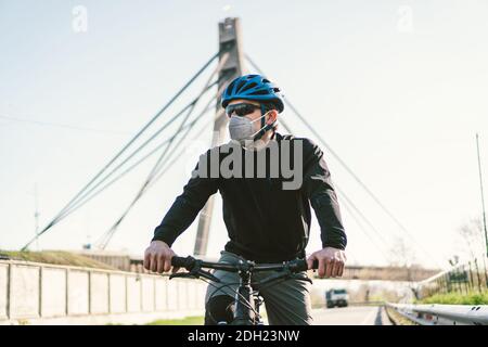 Männlicher Radfahrer trägt Atemschutzmaske mit strapazierfähigem Schutzfilter. Mann auf dem Fahrrad trägt Atemschutzmaske Gesichtsmaske mit schweren Stockfoto