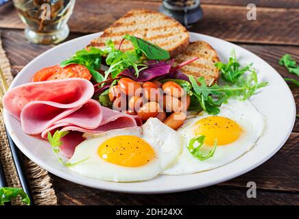 Englisches Frühstück - Spiegelei, Bohnen, Tomaten, Wurst, Schinken und Toast. Stockfoto