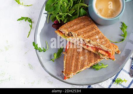 Gegrillte Club Sandwich Panini mit Rindfleisch, Tomaten, Käse, Salat und einer Tasse Kaffee. Leckeres Frühstück oder Snack. Draufsicht, Overhead, Flat Lay Stockfoto