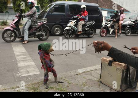 Gelernter Makake namens Undun mit Maske aus gebrochenem Puppenkopf und sein 17-jähriger Besitzer Latif treten an ihrem Arbeitsplatz an einer belebten Kreuzung in Surakarta in Zentral-Java, Indonesien auf. Straßenaufführungen mit wilden Affen, die als Topeng Monyet ('masster Affe' oder 'tanzender Affe') bekannt sind, sind in Indonesien trotz der Proteste von Tierrechtsaktivisten immer noch sehr beliebt. Langschwanzmakaken (Macaca fascicularis) werden normalerweise für diese grausame Praxis verwendet. Stockfoto