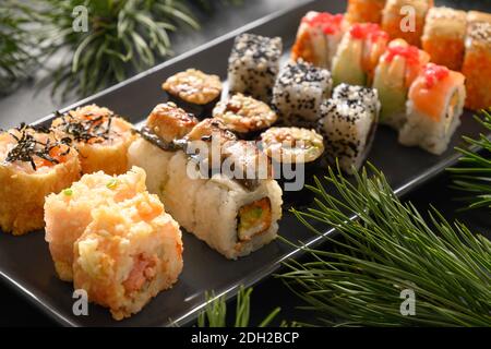 Weihnachtsessen mit Sushi-Set mit Weihnachtsdeko auf schwarzem Hintergrund. Nahaufnahme. Weihnachtsfeier oder Neujahrsparty. Stockfoto