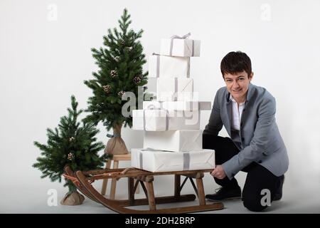 Weihnachts-themed horizontale Business-Porträt eines smart casual gekleidet weibliche Executive schieben einen Schlitten mit weißen und silberumhüllten Geschenkboxen auf einem grauen Hintergrund geladen. Stockfoto