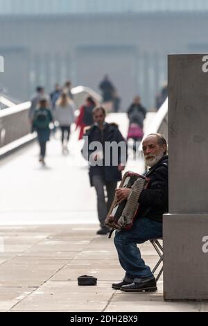 Ein alter Mann, der auf einem Akkordeon neben der Millennium Bridge, London, buschte Stockfoto