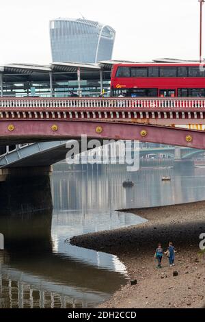 Zwei Frauen, die bei Ebbe am Ufer der Themse unter der Blackfriars Bridge entlang gehen, mit Walkie Talkie-Gebäude im Hintergrund, London Stockfoto