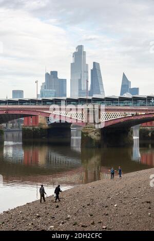 Menschen, die am Ufer der Themse bei Ebbe nahe der Blackfriars Bridge mit Blick auf die Stadt im Hintergrund spazieren, London Stockfoto