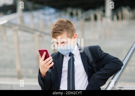 Schuljunge geht aus der Schule tragen Schutzmaske in der Stadt Stockfoto