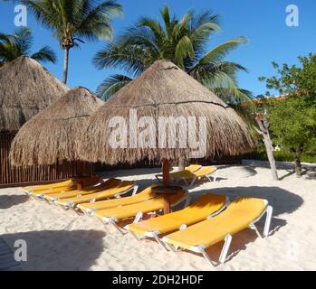 Strohschirme mit Palmwedel und Klappstühle für die Chaiselongue an einem Karibikstrand an der Riviera Maya in Cancun, Mexiko, für Reisehintergründe. Stockfoto