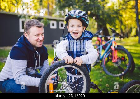 Vater's Tag kaukasischer Vater und 5 Jahre alter Sohn im Hinterhof in der Nähe des Hauses auf dem grünen Gras auf dem Rasen, der ein Fahrrad repariert, Stockfoto