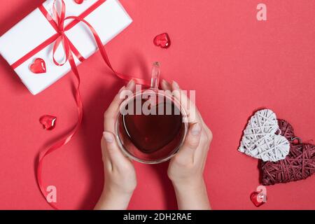 Frau Hände halten Tee Tasse in einem Herz mit roten Herzen Dekoration auf roten Tisch Draufsicht geformt. Konzept zum Valentinstag. Valentinstag romantisch Stockfoto