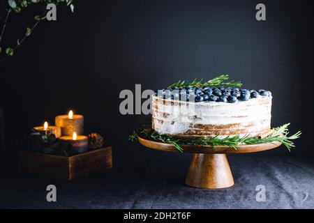 Schokoladenkuchen mit frischen Heidelbeeren verzierten Rosmarinzweig auf einem Holztablett in einem dunklen Innenraum. Stockfoto