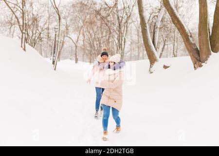 Zwei Mädchen spielen Schneebälle im Winter im Wald. Schwestern in einem warmen Kleid haben Spaß mit Schnee im Winter Stockfoto